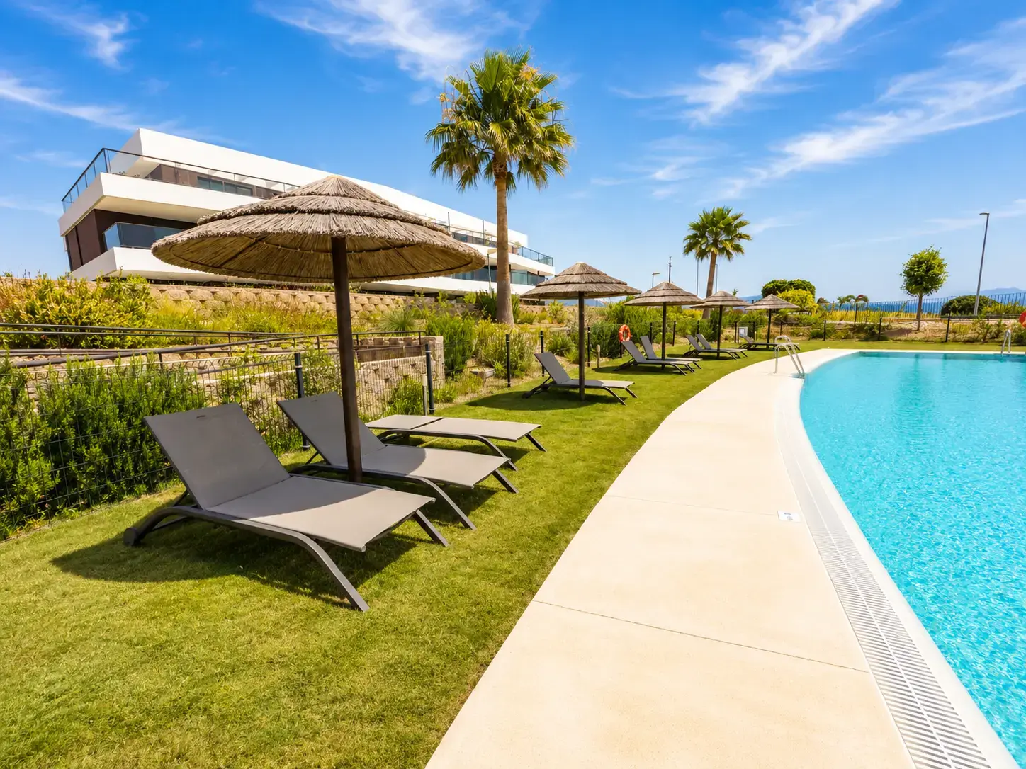 Sun loungers and parasols lining the community pool, with the residence and Mediterranean beyond — Estepona Golf Retreat