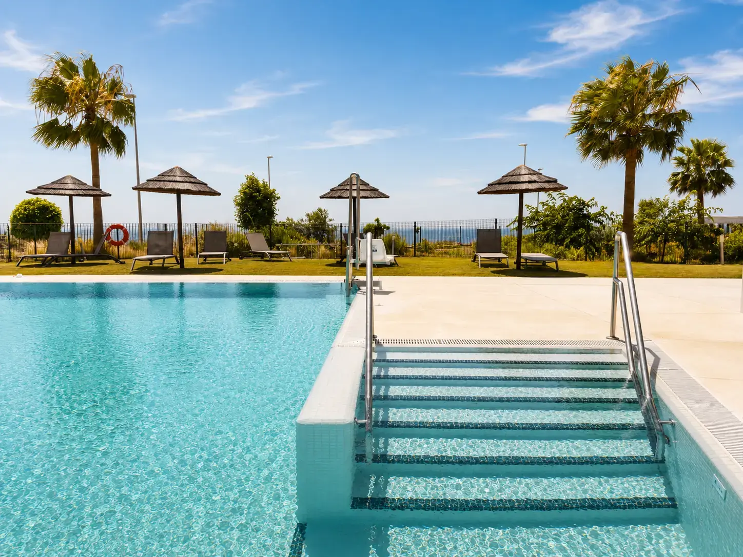Palms and sun loungers around the community pool overlooking the Mediterranean